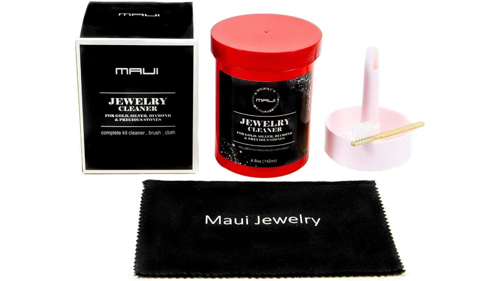 A red container of cleaning solution, a pink stand and brush sit behind a Maui Jewelry cleaning cloth.