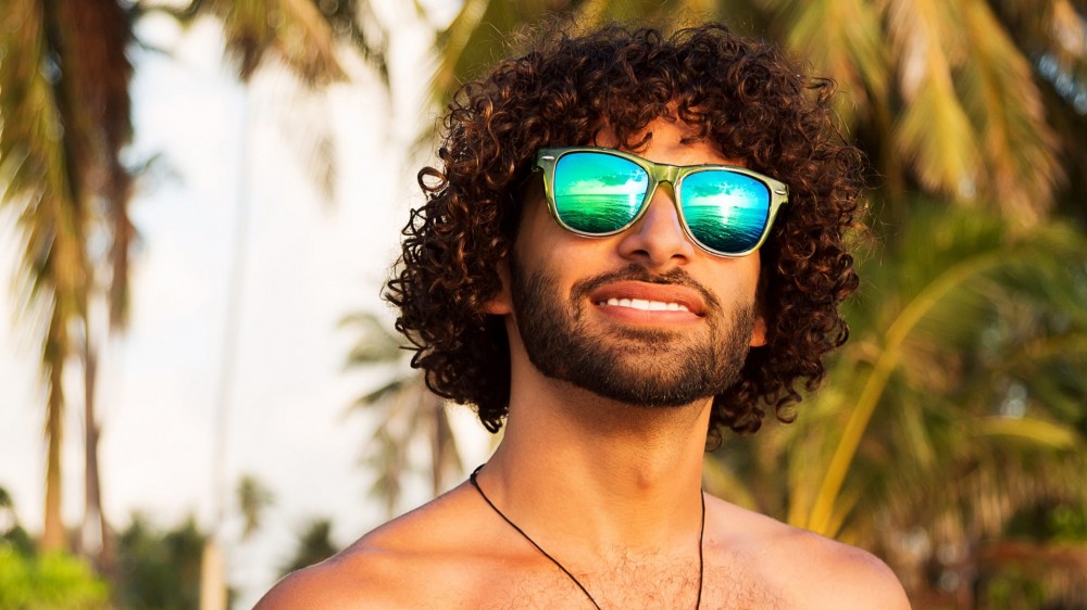 Young man wearing sunglasses outside with palm trees in the background.