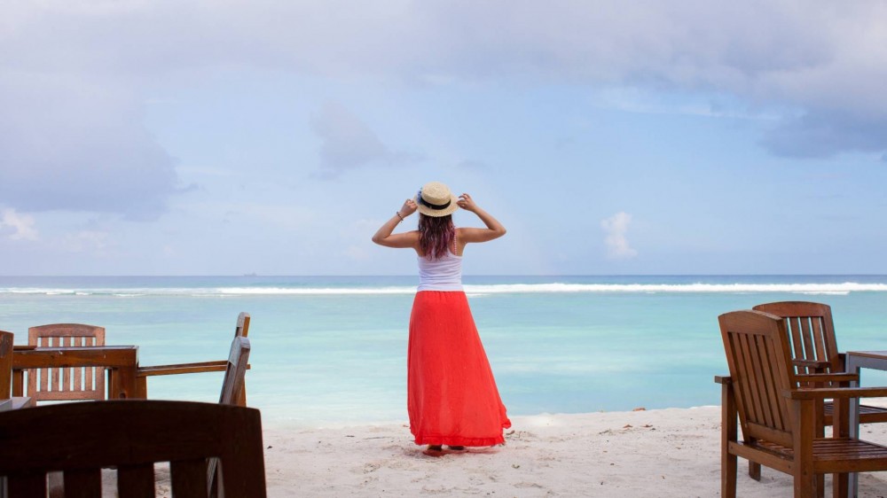 Woman standing near the ocean in a bright red skirt and white tank top.