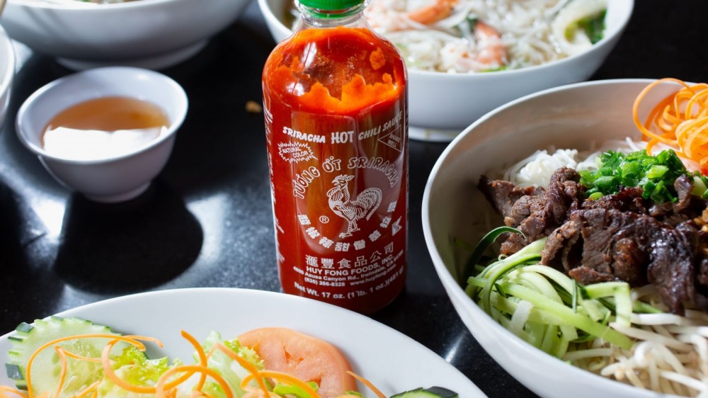 Bottle of sriracha on a table with asian dishes